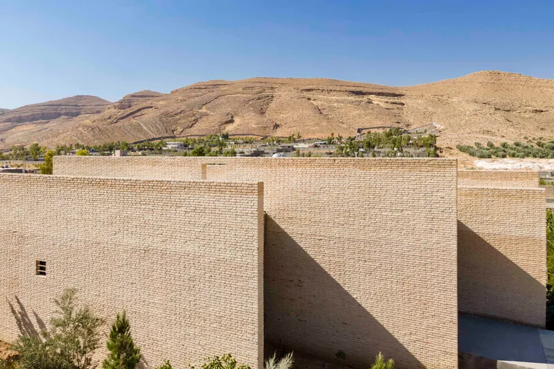 Clustered brick volumes with flat roofs set against a backdrop of barren rolling hills
