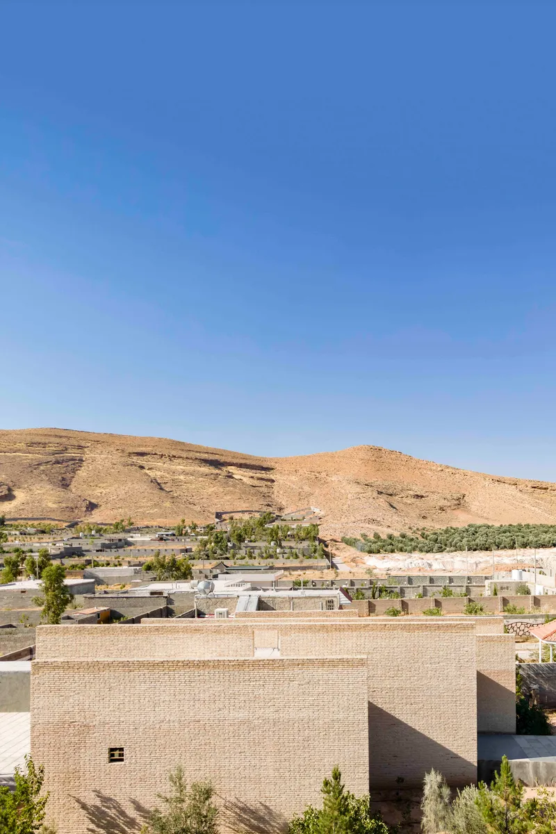 Rooftop view of the rectilinear brick structure amid a sparse settlement below arid mountains