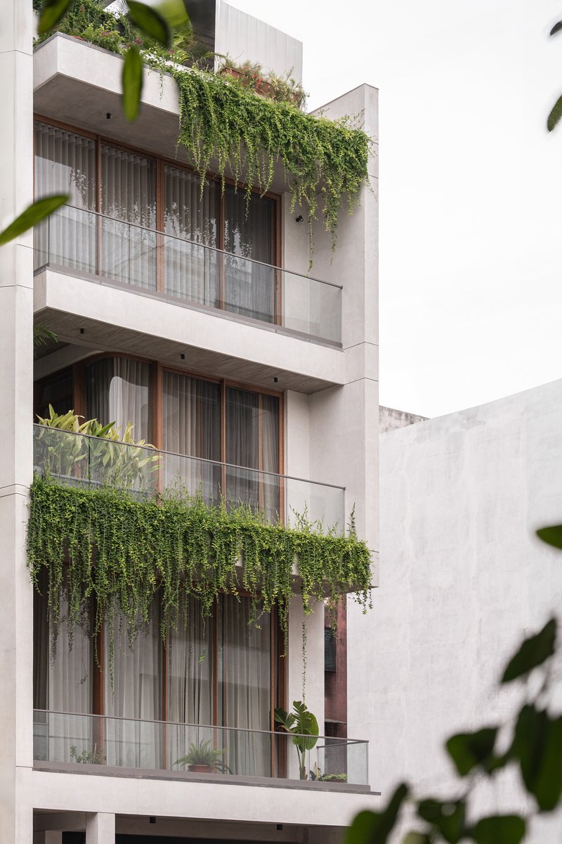 Street-facing facade with stacked balconies, timber screening and cascading greenery between floors
