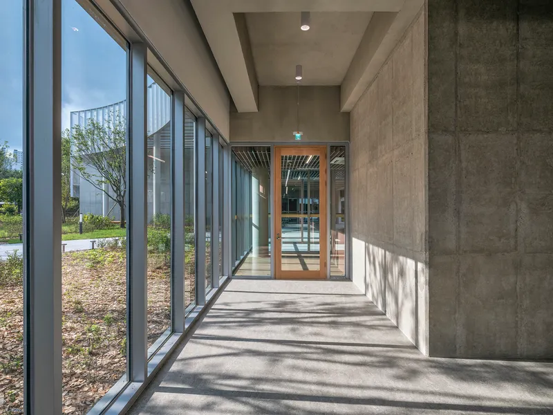 Glazed corridor with exposed concrete ceiling and dappled sunlight on the polished floor