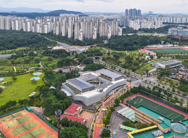 Aerial view of the white complex nestled between parkland tennis courts and surrounding tower blocks