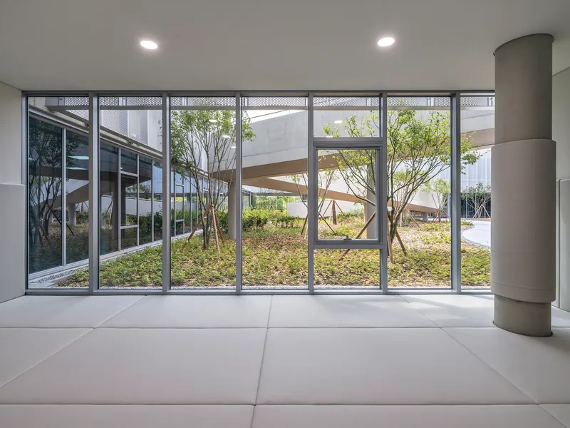 Glazed wall framing a view into the landscaped courtyard with young trees and planted beds