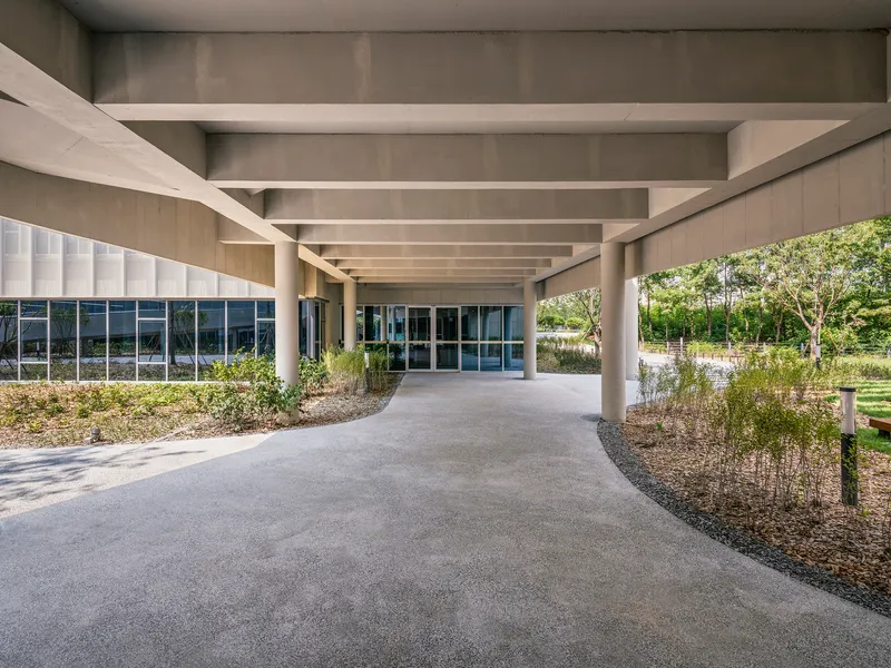 Entry portico with concrete beams sheltering the curved path and planted gravel beds beside glass doors