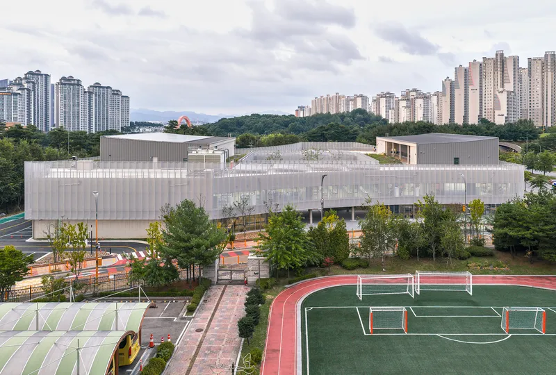 Elevated view of the white perforated metal facade with sports fields and residential towers beyond