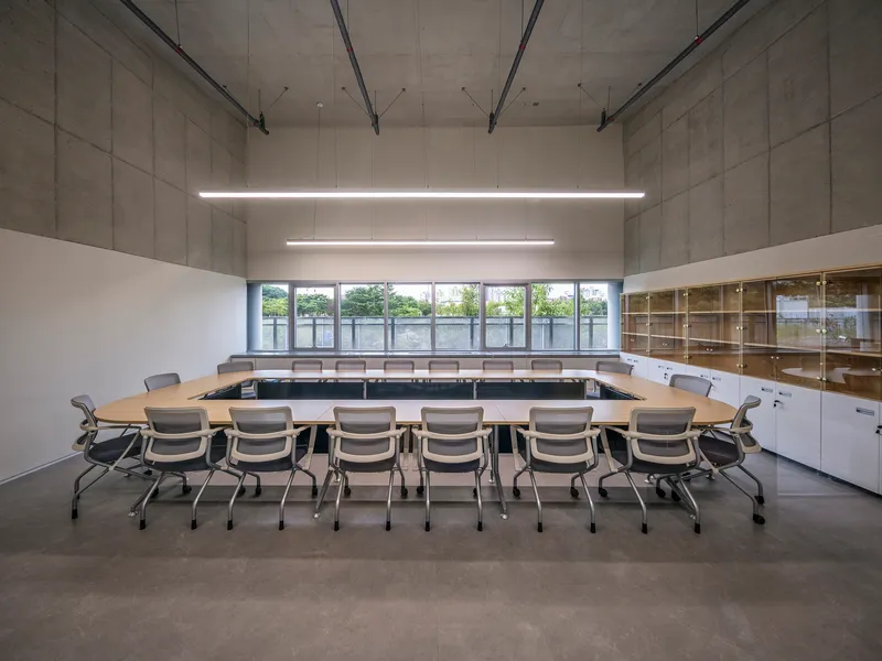 Conference room with U-shaped table arrangement under suspended linear lighting and exposed concrete ceiling