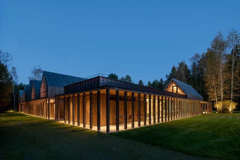 Corner view of timber colonnade wrapping the perimeter with illuminated interior spaces at night