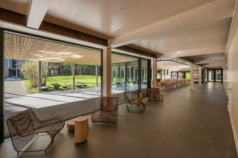 Interior circulation space with rattan lounge chairs opening to a courtyard through floor-to-ceiling glazing