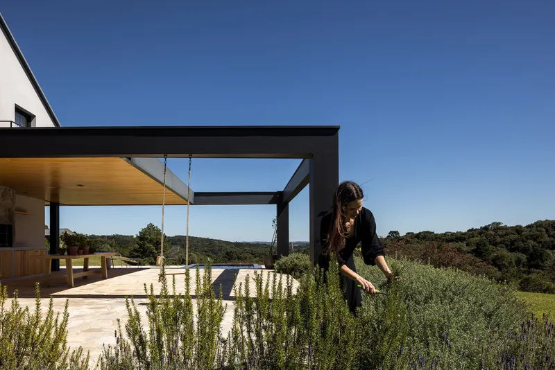 Rooftop terrace with black steel pergola, planted herbs and a figure tending the garden