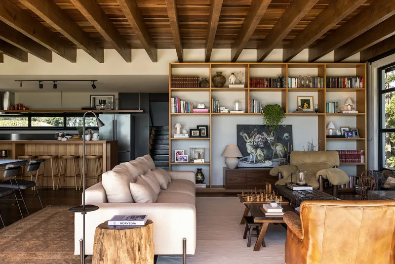 Open-plan living space with exposed timber structure linking built-in shelving, seating area, and kitchen beyond