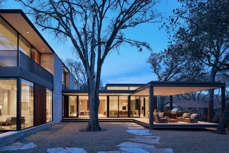 Courtyard view at dusk with three glazed volumes arranged around a preserved oak tree
