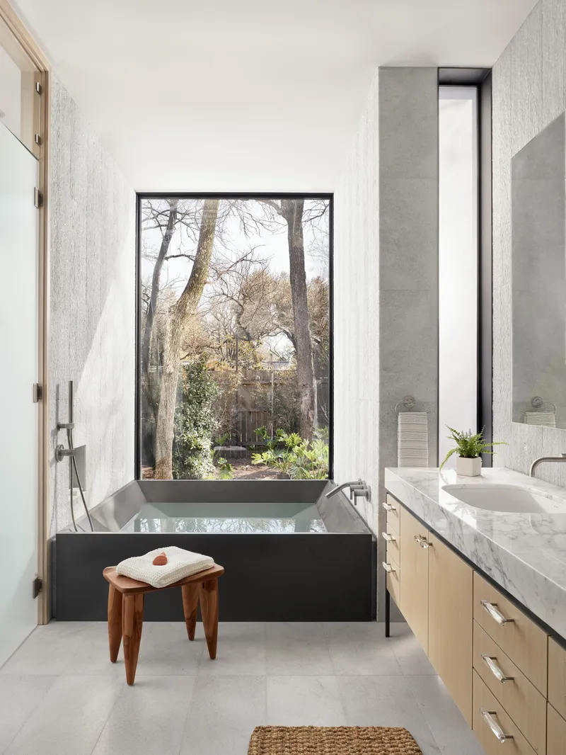 Bathroom with black soaking tub positioned beneath a tall window framing bare trees outside