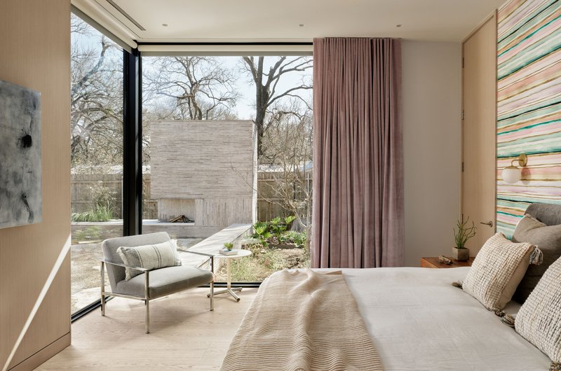 Bedroom with full-height glazing overlooking a courtyard garden under winter light