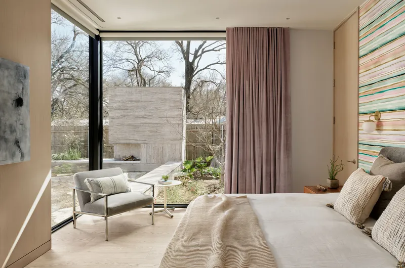 Bedroom with full-height glazing overlooking a courtyard garden under winter light