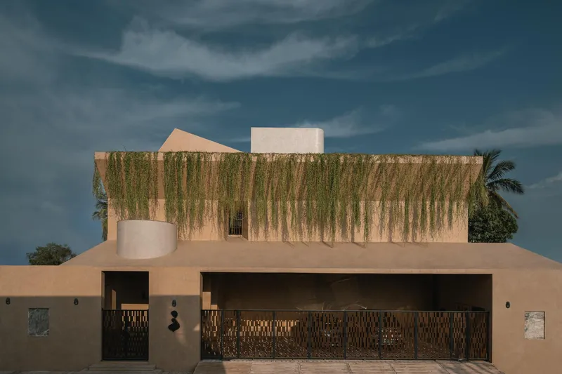 Street view of the residence with cascading greenery on upper facade and patterned metal screens at dusk