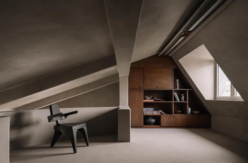 Attic workspace with exposed pitched ceiling beams and a built-in timber bookshelf under a triangular window
