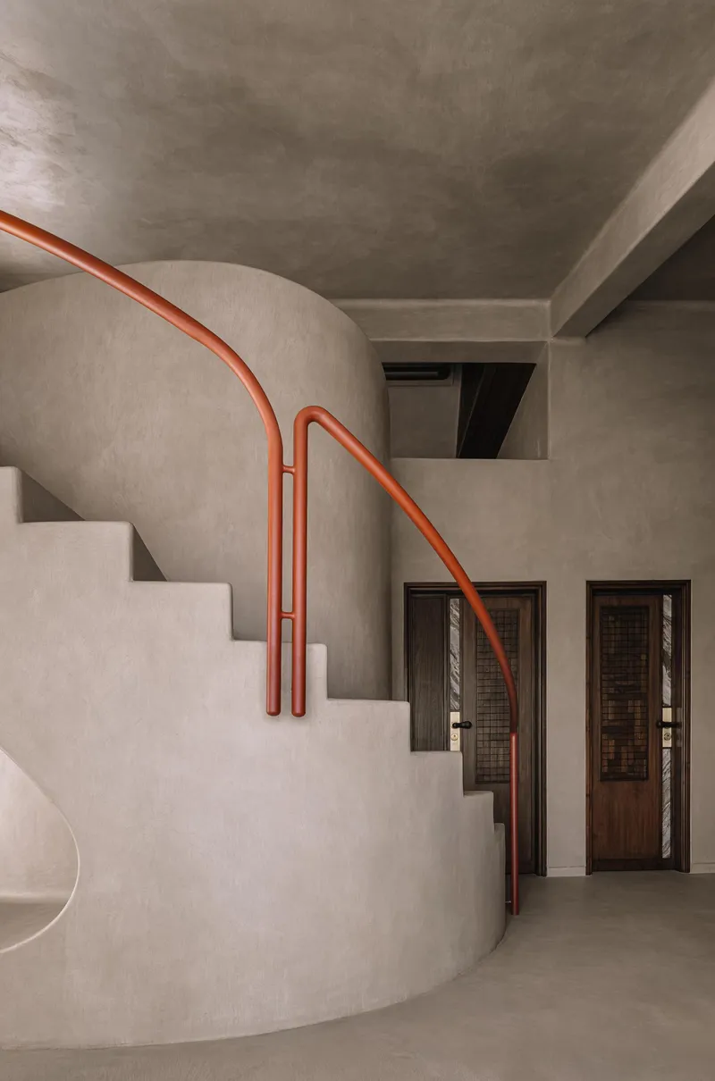 Curved stair with orange tubular handrail descending past doorways with woven panel inserts