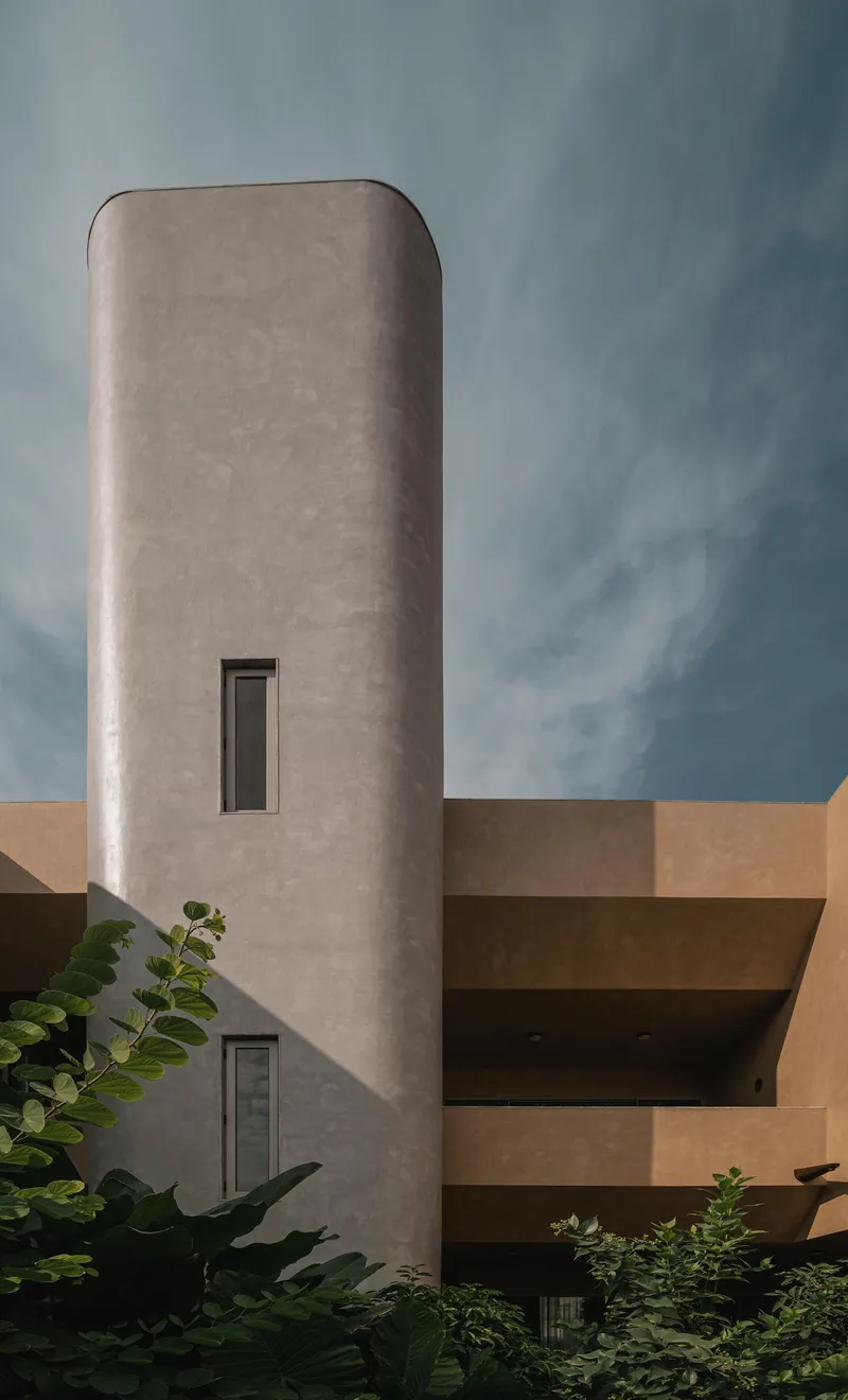 Cylindrical concrete tower with narrow vertical windows and foliage at its base