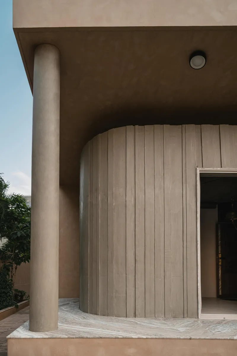 Covered entry with cylindrical concrete column and curved vertical timber wall under a clear sky