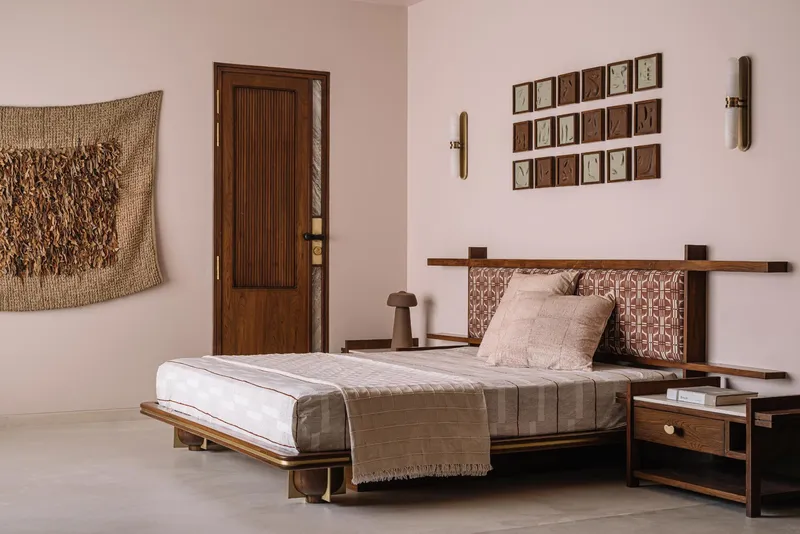 Bedroom with low platform bed, woven wall hanging and grid of framed artworks in natural light