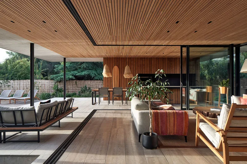 Open plan living space with timber slat ceiling and glazed walls facing the pool deck