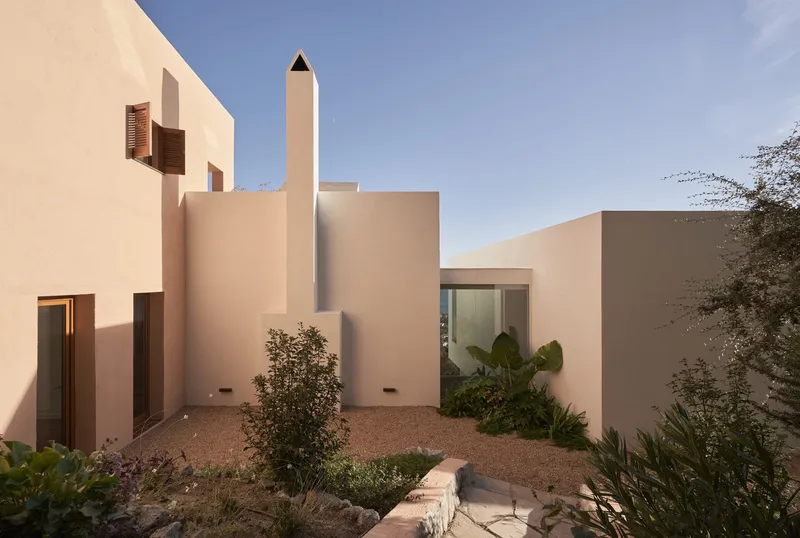 Courtyard with tall cylindrical chimney rising above clustered stucco volumes with desert plantings