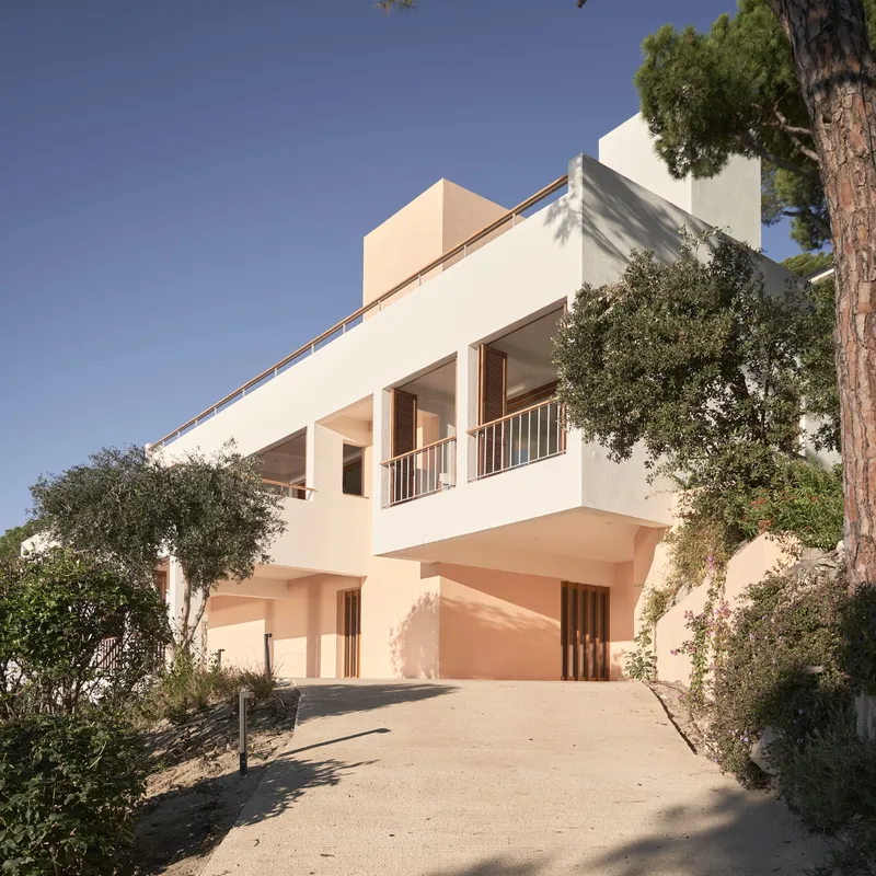 Sloped driveway approach to stucco facade with timber balcony and vertical slat screening