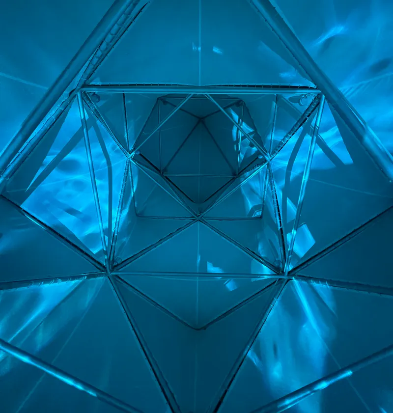 Interior view looking up through blue-lit triangulated glass and steel framework creating kaleidoscopic reflections
