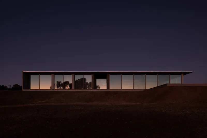 Long glazed facade illuminated from within at twilight against the dark hillside and deepening blue sky