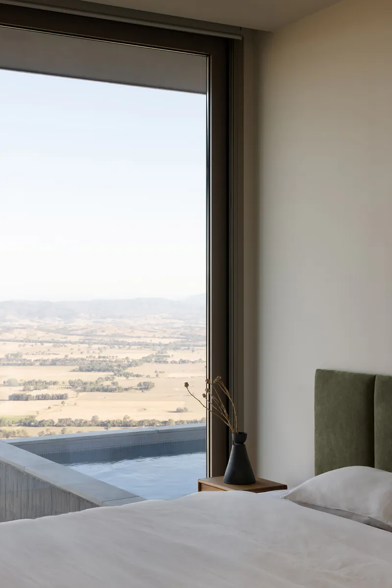 Bedroom window framing a hazy valley view with a tiled pool edge visible outside
