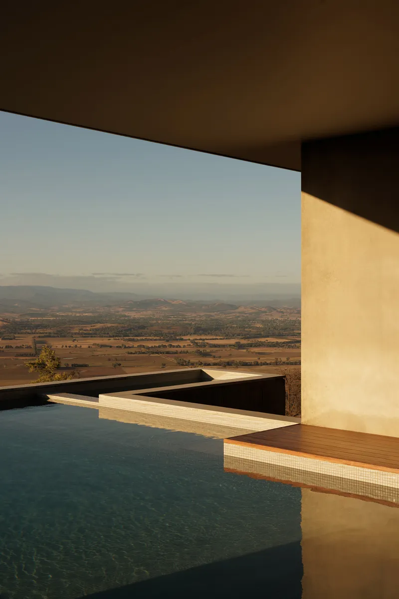 Pool terrace edge with white rendered wall casting shadow across water at sunset