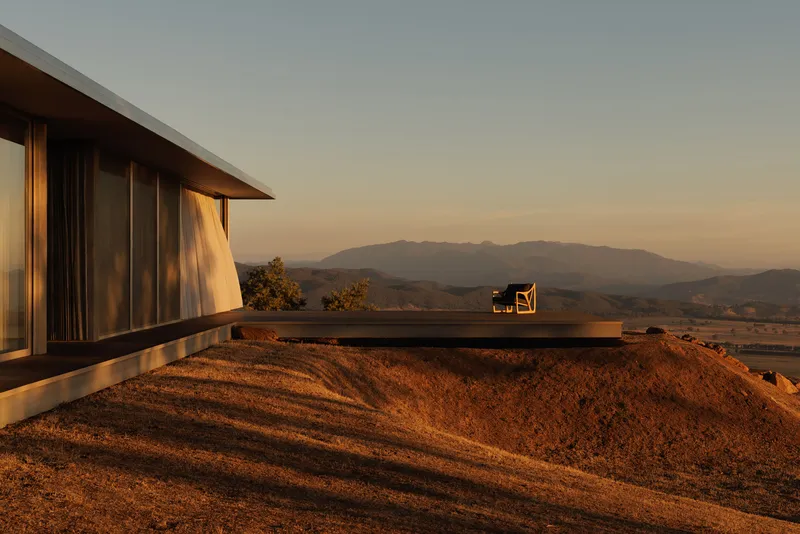 Cantilevered terrace perched above excavated hillside with mountain range visible at dusk