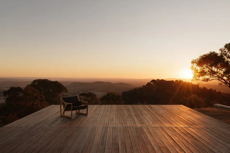 Timber deck with solitary lounge chair facing distant mountains and trees at sunrise