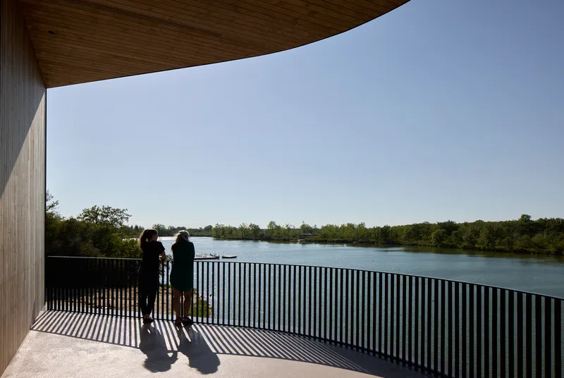 Covered terrace with vertical black railing and two visitors looking out toward wooded lakeshore
