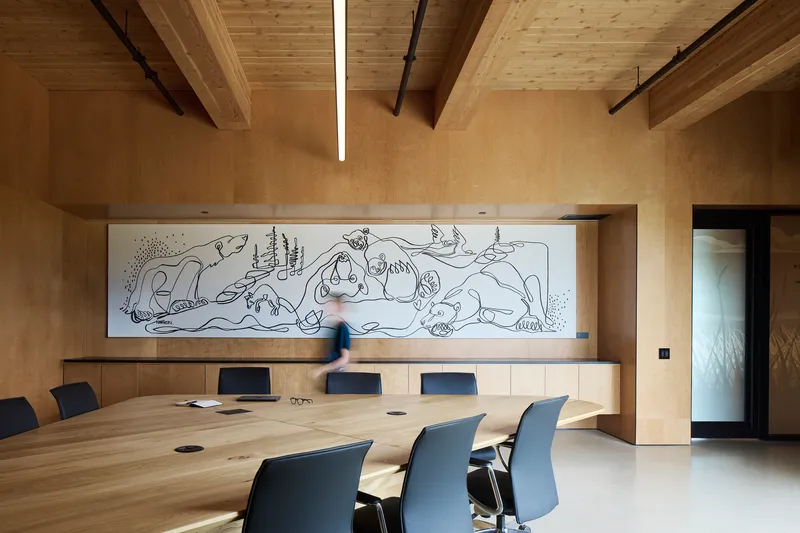 Conference room with long timber table and wall mural under exposed beam ceiling with linear lighting