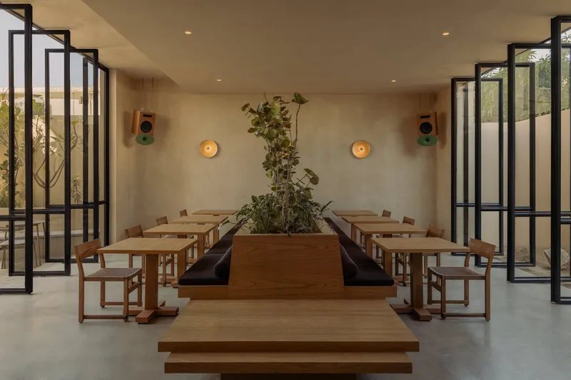 Interior dining room with timber tables flanking a central planter and steel-framed glass doors