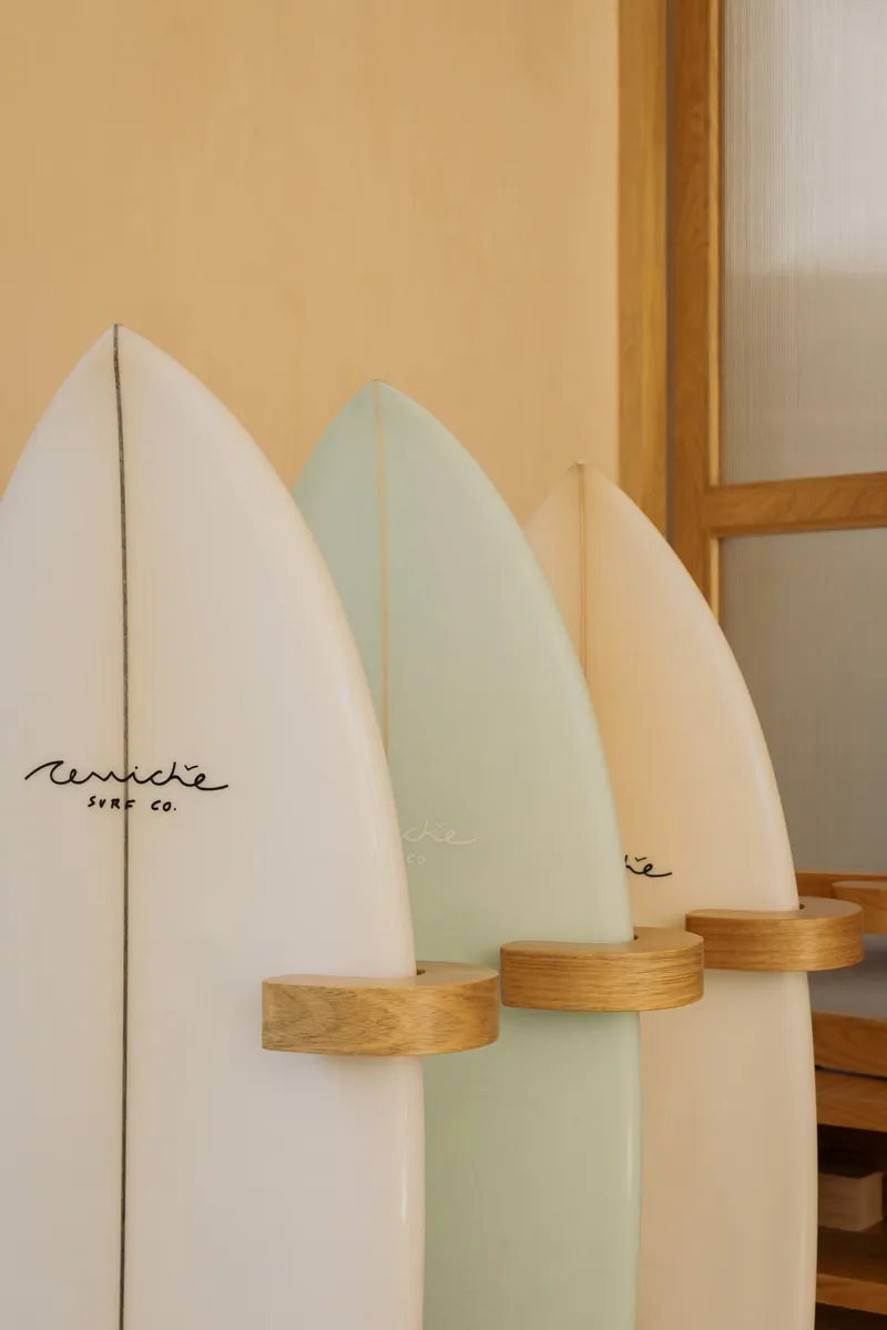 Three surfboards mounted on wooden pegs against a pale plywood wall and glass partition