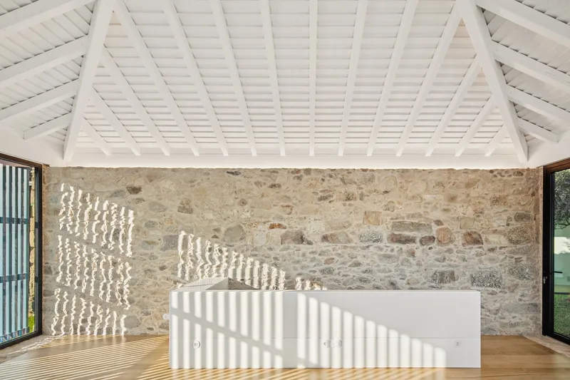 Interior with exposed stone wall and white painted timber ceiling casting striped shadows across wooden floor