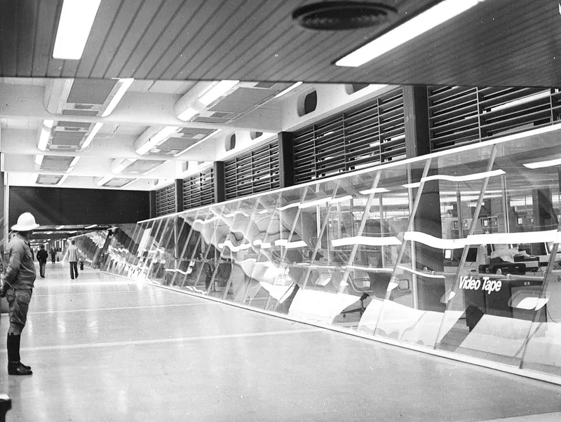 Interior hall with angled white structural frames and overhead arrival departure boards with visitors walking
