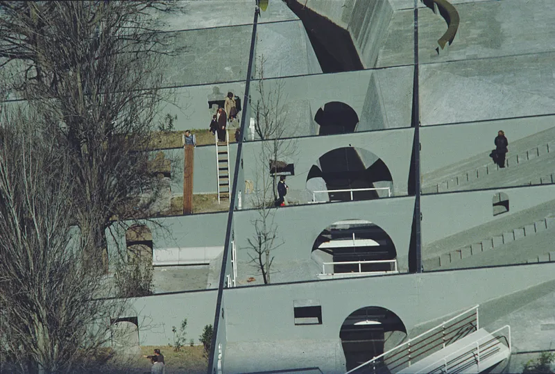 Sloped green facade with circular window openings and workers on ladders during installation