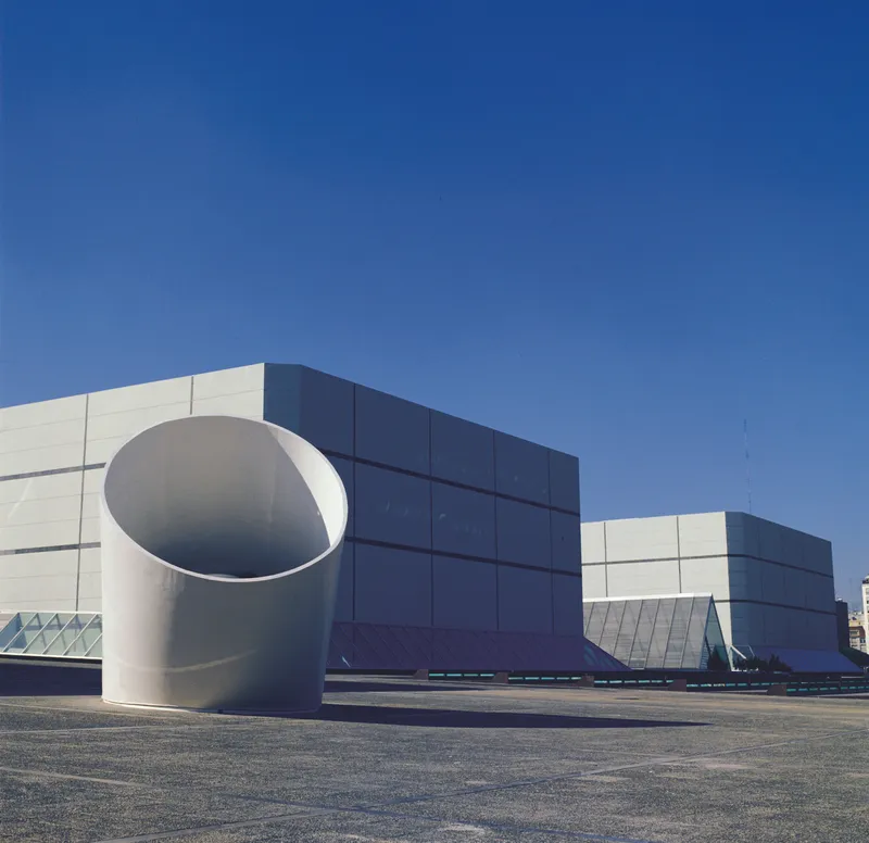 Blue and white paneled facade with large cylindrical volume under a clear sky