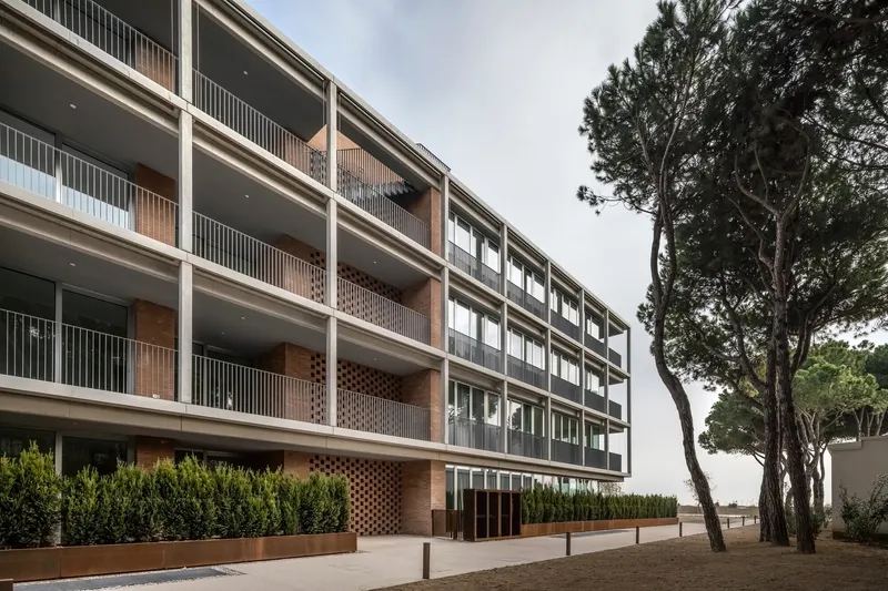 Street-facing elevation with concrete frame balconies, perforated brick screens and planted hedge at ground level