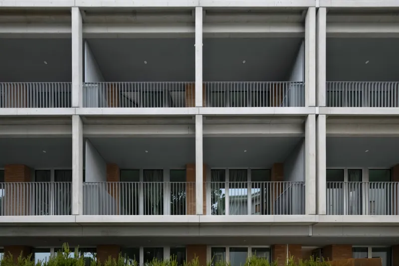Concrete structural grid facade with recessed balconies lined with vertical timber slats and metal railings
