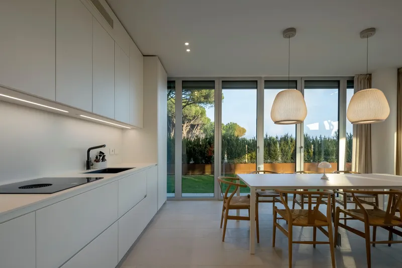 Open-plan kitchen and dining area with full-height glazing opening to a garden at dusk