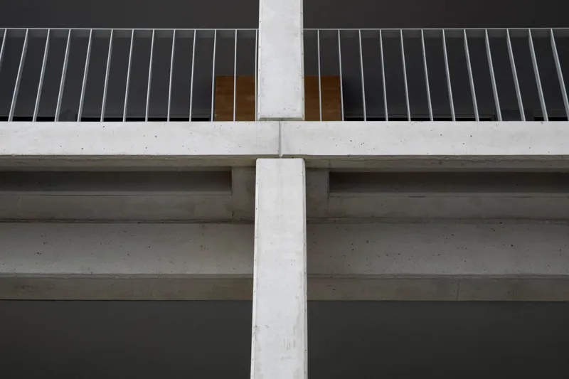 Underside view of concrete balcony slabs meeting a vertical column with vertical metal slat railing above