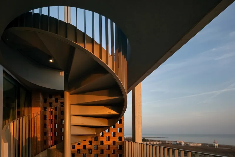 Spiral staircase with vertical slat screen and perforated brick wall at dusk with ocean view beyond