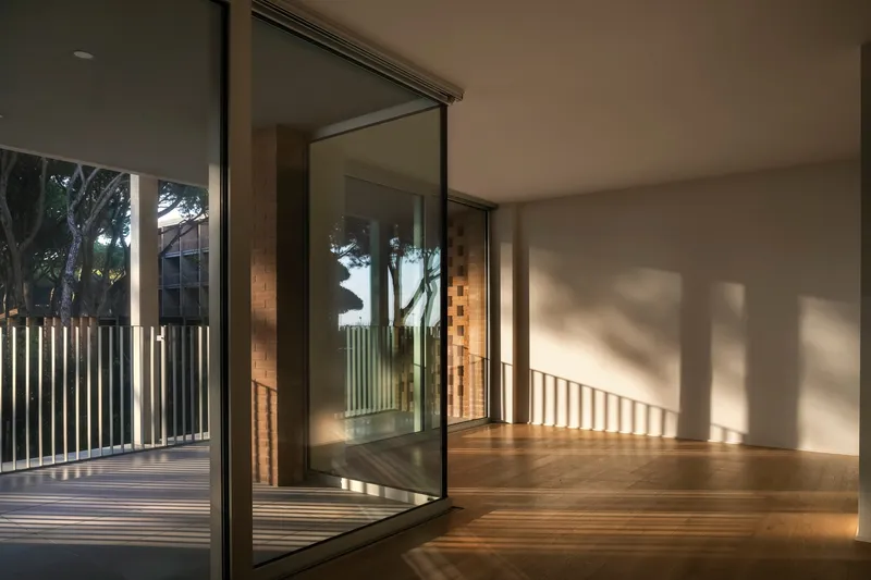 Interior room with timber floor and glass doors opening to terrace with striped sunlight shadows