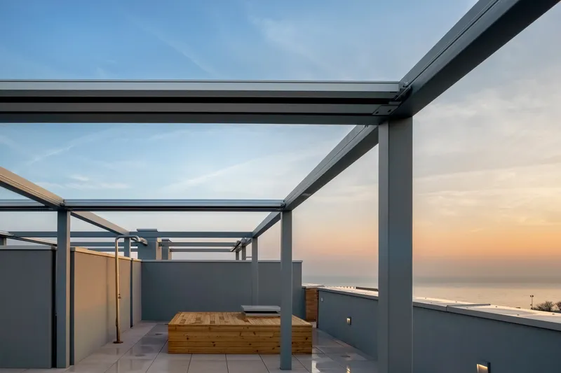 Rooftop terrace with steel frame pergola and timber seating overlooking the sea at dusk