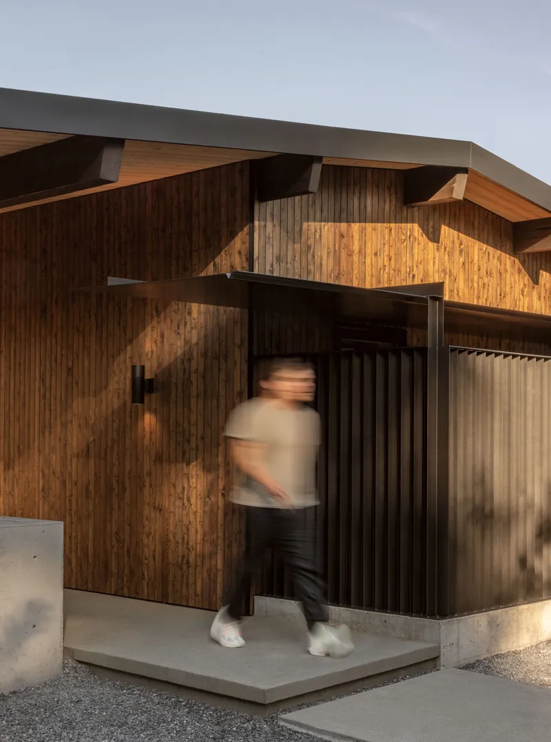 Entry threshold with vertical timber cladding and concrete base as a person moves through the doorway