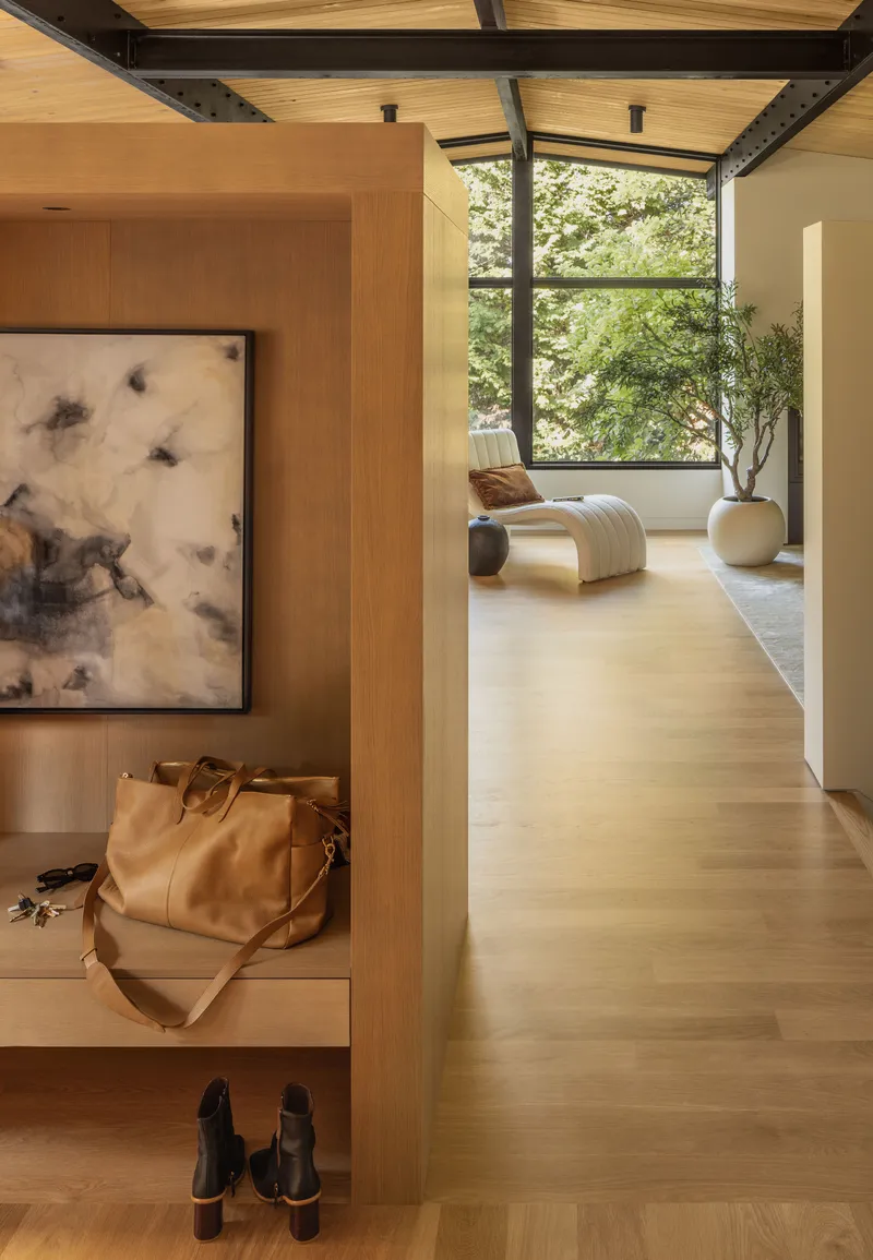 Entry niche with timber storage and framed artwork opening to a daylit hallway beyond