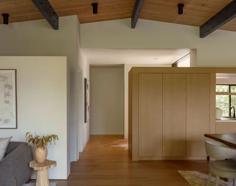 Living space with freestanding timber storage volume connecting to kitchen under exposed ceiling beams